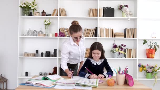 Mother in glasses helping brunette daughter to do homework at home — Stock Video