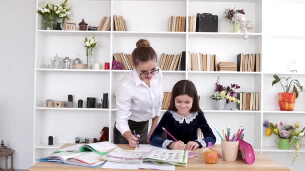 Mother in glasses helping brunette daughter to do homework at home