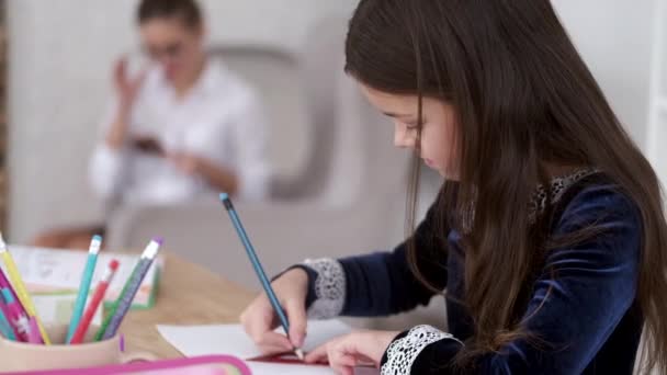 Ребенок делает домашнее задание, пока мама по телефону — стоковое видео