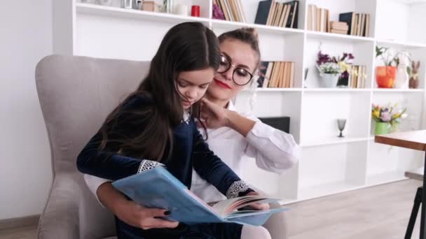 Colegiala lectura libro con mamá en apartamento moderno — Vídeos de Stock