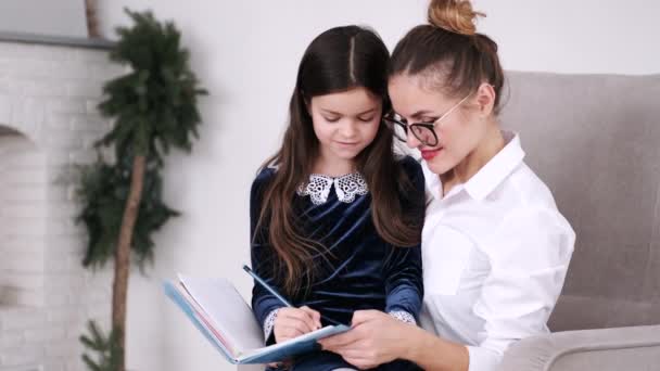 Schulmädchen liest Buch mit Mama in moderner Wohnung — Stockvideo