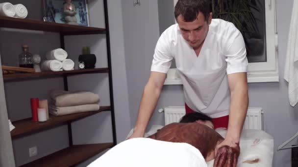 Masseur in uniform massages klanten terug met masker — Stockvideo