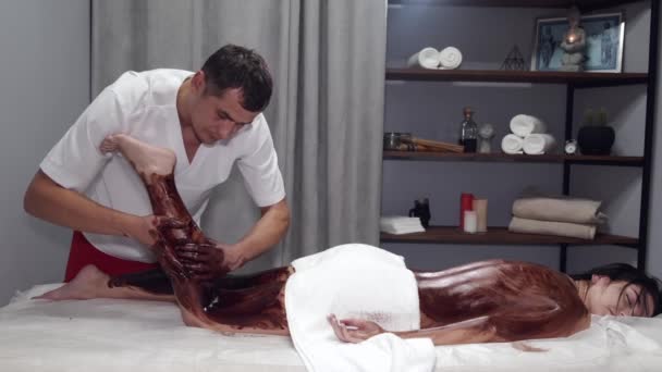 Masseur massaging woman legs with brown mask — Stock Video