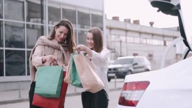 Mutlu kız arkadaşlar alışveriş yaptı ve el işi alışveriş çantalarını bir arabanın bagajına koydu.