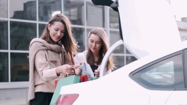Щасливі подружки розкупилися і поклали крафтові сумки в багажник автомобіля — стокове відео
