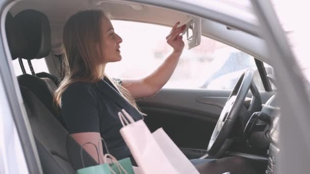 En vacker kvinna sitter i en bil och tittar på en bilspegel. — Stockvideo