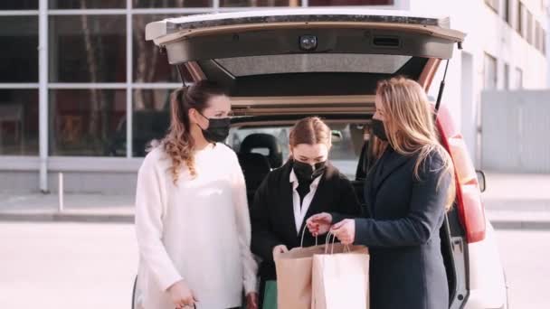 Maskeli üç kız bir arabanın yanındaki alışveriş çantalarına bakıyor. — Stok video