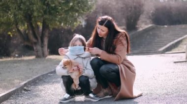 Avrupalı anne ve maskeli kızı bir köpekle parktalar.