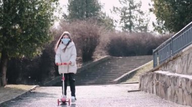 Koruyucu maskeli kız parkta scooter kullanıyor.