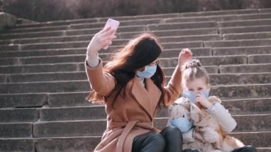 Maskeli anne ve kız merdivenlerde selfie çekiyorlar.