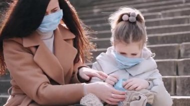 Maskeli anne ve kız, maske takan oyuncak bir oyuncak bebek gösteriyorlar..