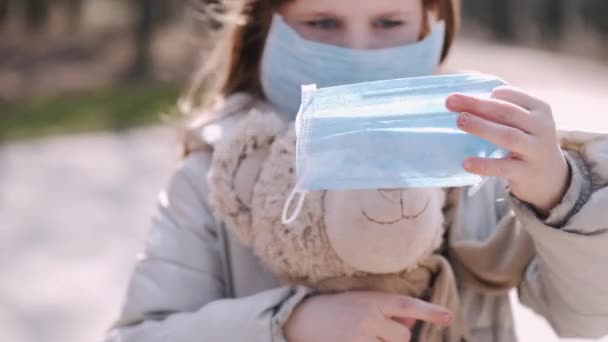 Девушка в маске надевает маску на игрушку плюшевого медведя — стоковое видео