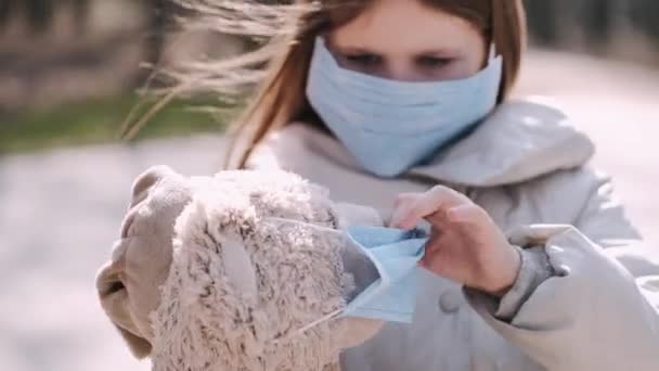 Het meisje met een masker zet een masker op teddybeer speelgoed — Stockvideo