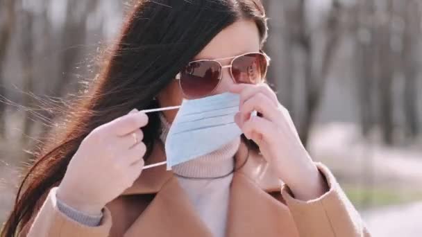 Mulher de casaco está a colocar uma máscara protectora no exterior — Vídeo de Stock
