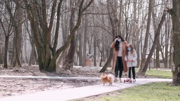 Az európai anya és a lánya maszkban egy parkban vannak egy kutyával. — Stock videók