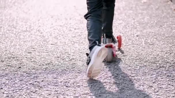 O miúdo está a conduzir uma scooter no beco do parque. — Vídeo de Stock