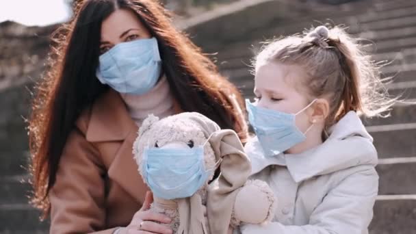 마스크를 쓴 엄마와 딸은 마스크를 쓴 테디 베어 장난감을 보여 주고 있다.. — 비디오