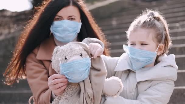 De moeder en dochter in maskers tonen een teddybeer speeltje in een masker. — Stockvideo