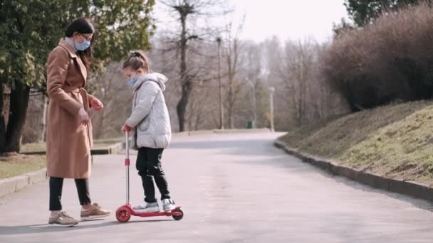 Mãe e filha em scooter usando máscaras estão andando no parque com um cão — Vídeo de Stock