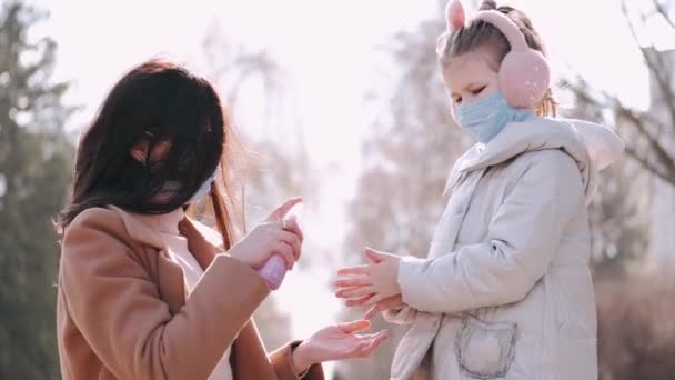 La madre está rociando líquido antiséptico en las manos de las hijas en un parque — Vídeos de Stock