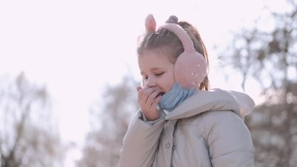 Kışın kulaklık takan ve maskeli çocuk dışarıda öksürüyor. — Stok video