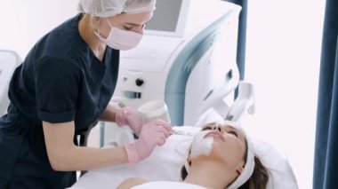 Kozmetik uzmanı kızların yüzüne güzellik salonunda krem sürüyor.