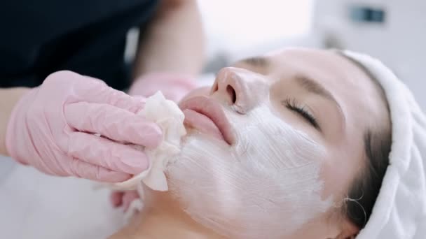Обрізаний вид косметолога, що видаляє маску для обличчя з обличчя — стокове відео