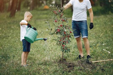 Küçük oğlu olan baba bahçeye ağaç dikiyor.