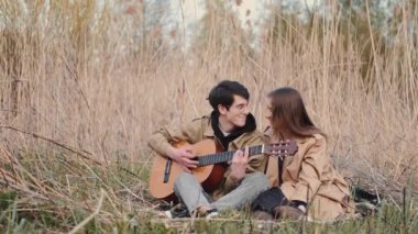 Gitarlı bir çocuk ve tarlada oturan bir kız.