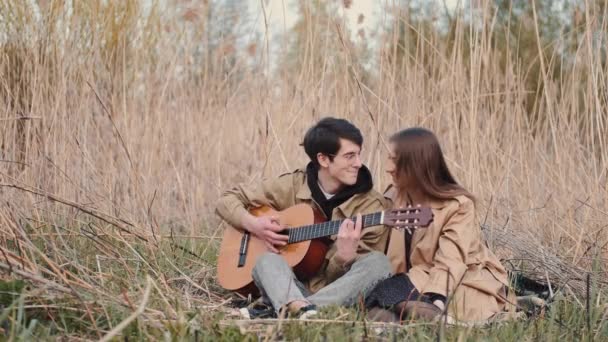 Junge mit Gitarre und Mädchen sitzen im Feld und haben Date — Stockvideo