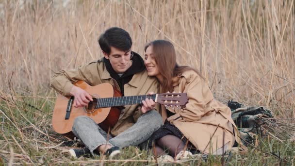 Chłopiec z gitarą i dziewczyna siedzi w polu i mając datę — Wideo stockowe