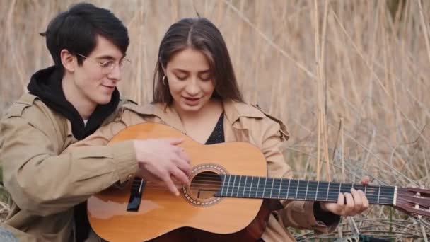 Menino ensinando menina como tocar música na guitarra no campo — Vídeo de Stock