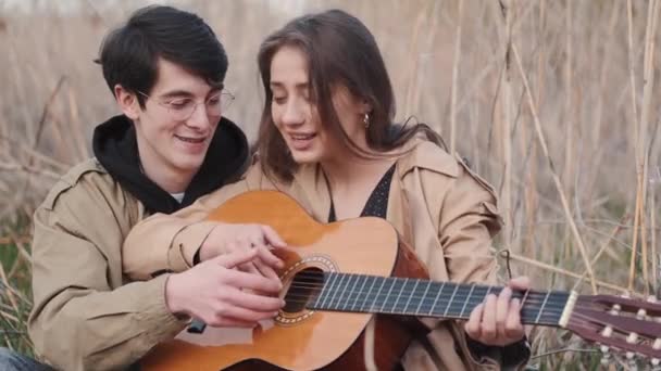 Хлопчик навчає дівчину грати пісню на гітарі в полі — стокове відео
