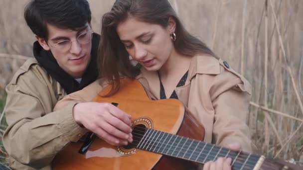 Αγόρι διδάσκει κορίτσι πώς να παίξει τραγούδι στην κιθάρα στον τομέα — Αρχείο Βίντεο
