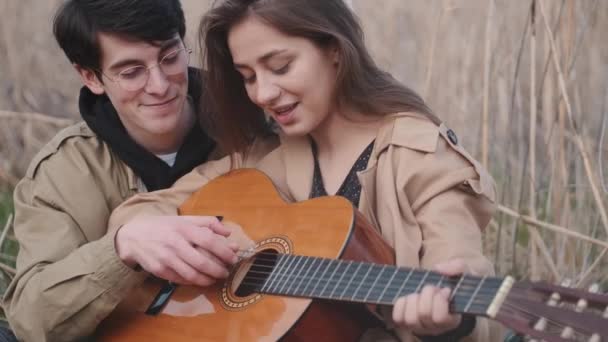 Chlapec učí dívku, jak hrát píseň na kytaru v poli — Stock video