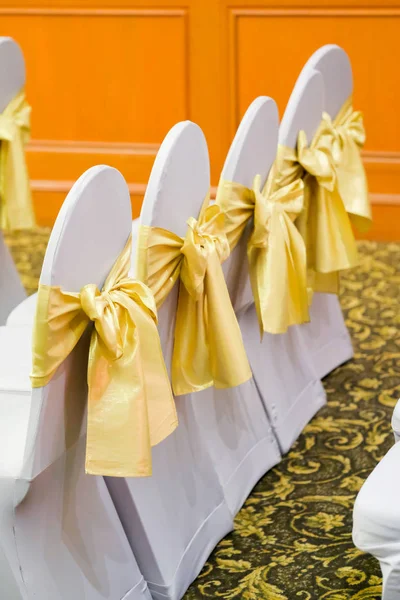 Row of white chairs decorated with gold ribbons