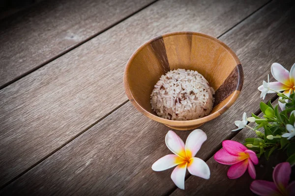 Vařená rýže v dřevěné misce a květiny na stole — Stock fotografie