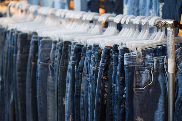 Row of Jeans and trousers on hangers for sale.