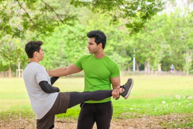 Two active man in sportswear stretching two in the park, front v