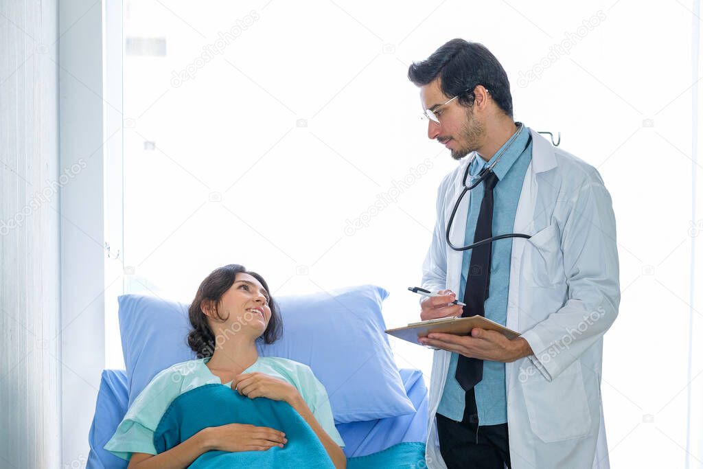 Front view of Caucasian male doctors and female patients, talking about illness and taking notes in the ward at the hospital