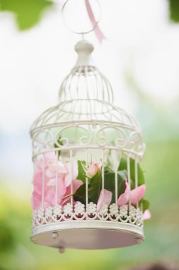Pembe çiçekler içinde güzel antika kuş kafesi.