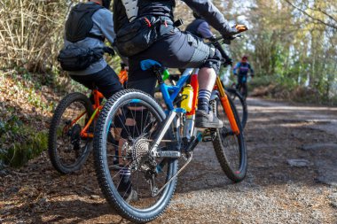 Ön planda, dağ bisikletlerinin üzerinde duran iki bisikletçi, antrenmana başlamadan önce gruptaki diğer sporcuların gelmesini bekliyor..