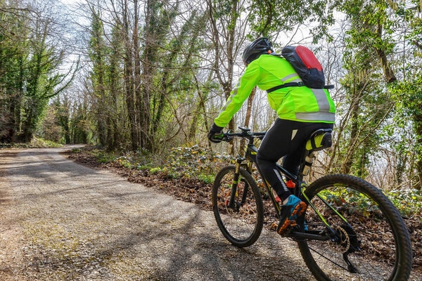 Rocca di Papa, Italy - February 29, 2020: A man rides a mountain bike on the country path. Daytime scene with the cyclist in the foreground and the vegetation with beech trees in the background. Backlit.