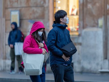 Rome, Italy - March 4, 2020: Asian tourists stroll in the center wearing a protective mask on their face. Coronavirus emergency in the city.
