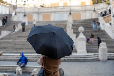 Rome, Italy - March 04, 2020: Woman with umbrella in Piazza di Spagna, on a gloomy day, sheltering from the rain.