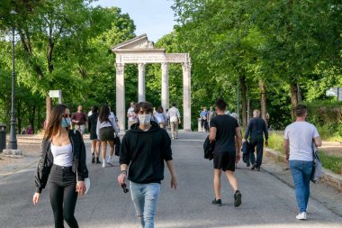 Roma, İtalya - 10 Mayıs 2020: Villa Borghese, halk parkında koruyucu maskeler takarak yürüyen insanlar. Coronavirüs salgınına yönelik kısıtlamaların hafifletilmesinden sonraki ilk pazar..