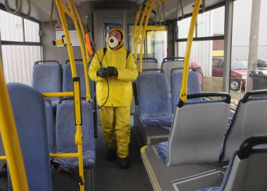 Koruyucu ekipman kullanan bir işçi, 13 Mart 2020 'de Kiev' deki otobüs durağında Coronavirus Covid-19 'a karşı önleyici tedbir olarak yolcu otobüsünü dezenfekte etmek için dezenfektan sıkar..