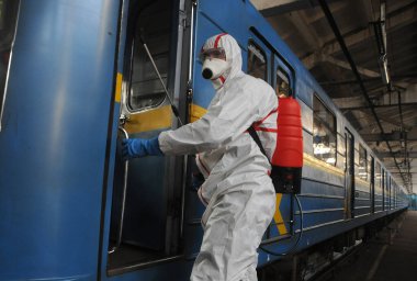 Koruyucu ekipman işçisi 16 Mart 2020 'de Kiev' deki otobüs durağında Coronavirus Covid-19 'a karşı önleyici önlem olarak Kiev Metro arabalarının dezenfekte edilmesi için dezenfektan sıkar..