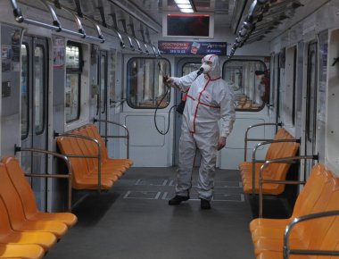 Koruyucu ekipman işçisi 16 Mart 2020 'de Kiev' deki otobüs durağında Coronavirus Covid-19 'a karşı önleyici önlem olarak Kiev Metro arabalarının dezenfekte edilmesi için dezenfektan sıkar..