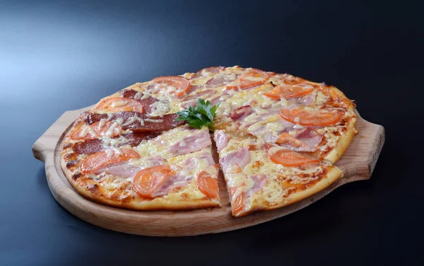 Pizza with tomatoes, cheese, meat and fish on dark background